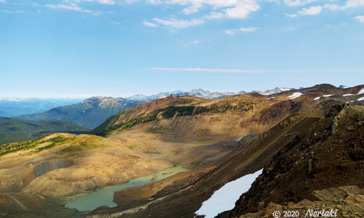 Cinder Cone が写真左下方に丘程度に見え、その手前に氷河が岩を削り岩紛が多量に入った池が確認出来ます。